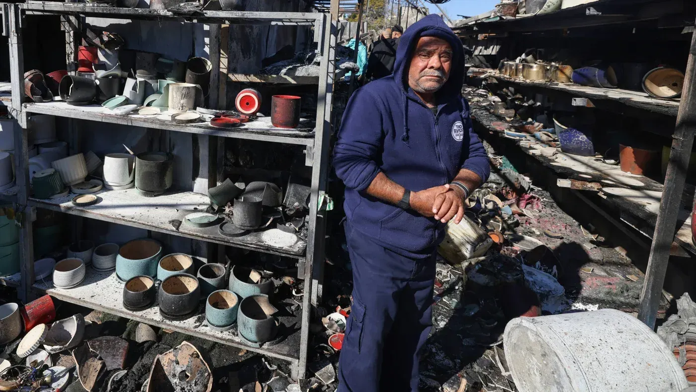 رجل فلسطيني يقف بين رفوف مدمرة مليئة بالأواني المحطمة، تعكس آثار اعتداءات المستوطنين في الضفة الغربية.