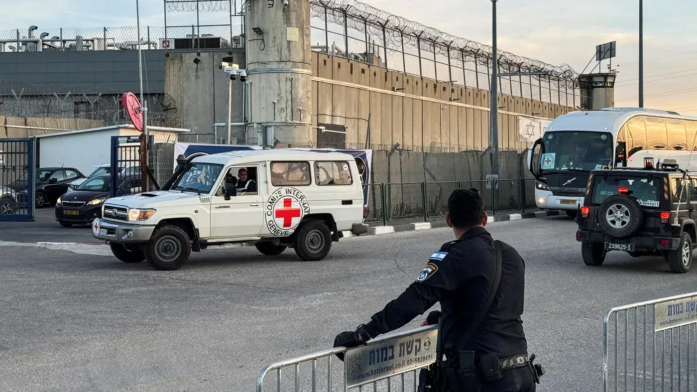 سيارة تابعة للصليب الأحمر تمر أمام سجن محاط بأسلاك شائكة، حيث يُظهر الوضع الأمني المشدد في مراكز احتجاز المعتقلين الفلسطينيين.