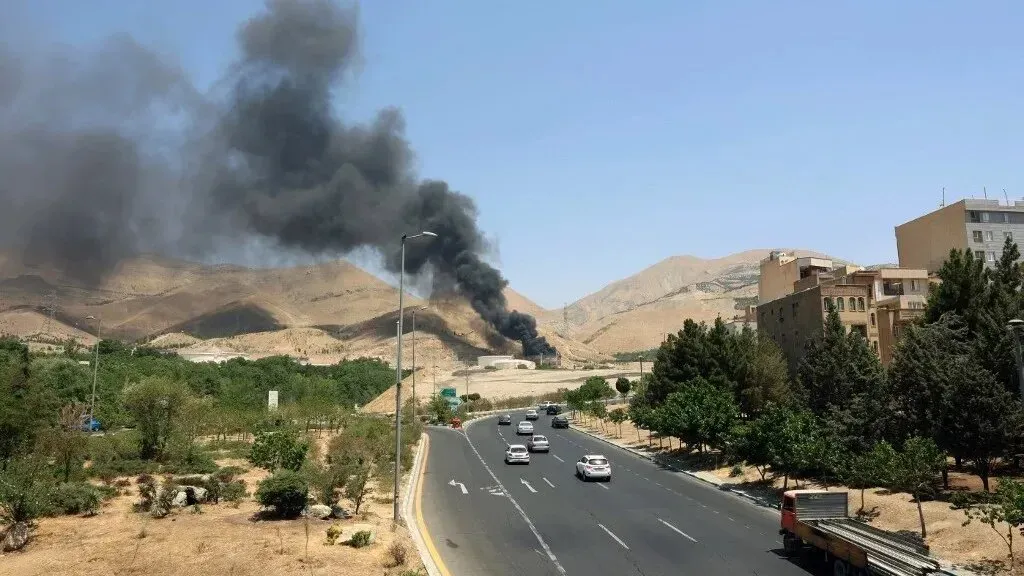 تصاعد دخان أسود كثيف من موقع غارة إسرائيلية في غرب إيران، مع تضرر المنطقة المحيطة ووجود سيارات على الطريق.