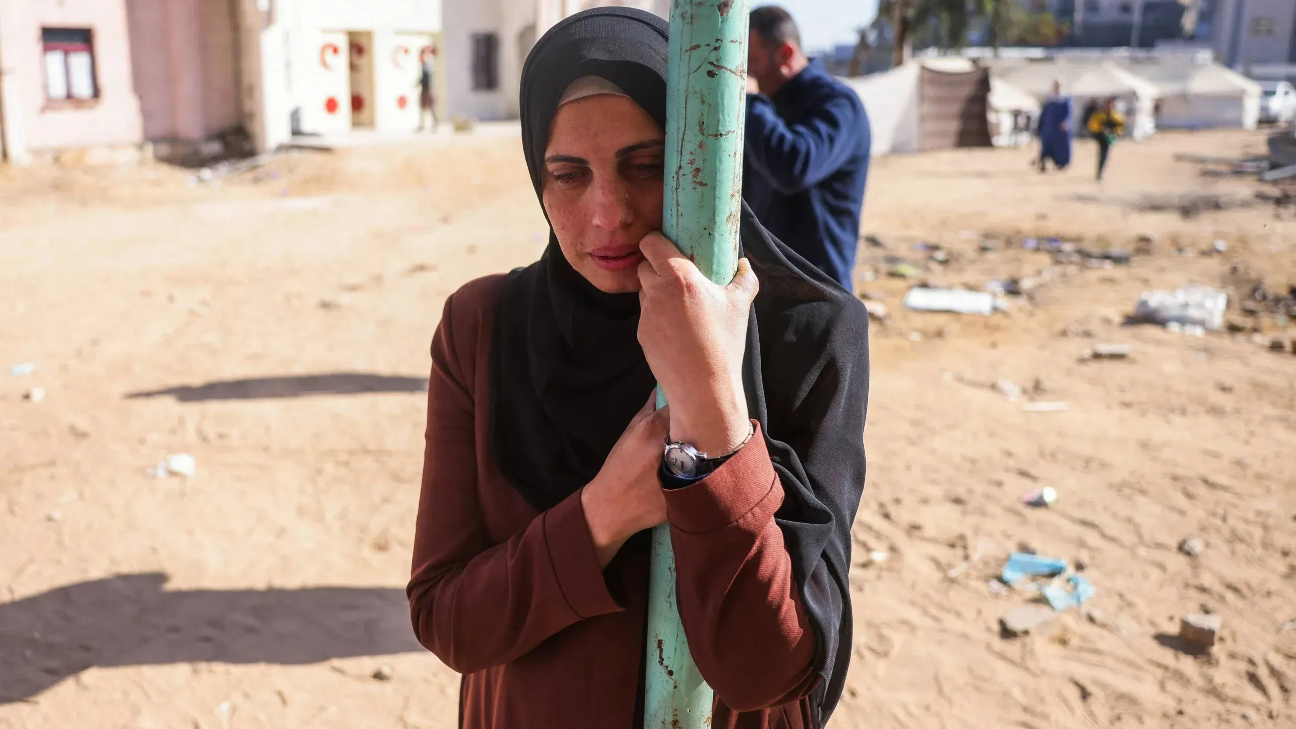 امرأة فلسطينية تحتضن عمودًا في مخيم للنازحين، تعبيرها يعكس الحزن والمعاناة جراء الغارات الإسرائيلية على غزة.