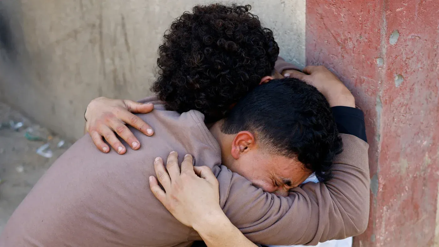 شابان يحتضنان بعضهما في لحظة حزن، تعبيراً عن ألم الفقدان في ظل تصاعد العنف في غزة، حيث قُتل 10 فلسطينيين في غارة إسرائيلية.