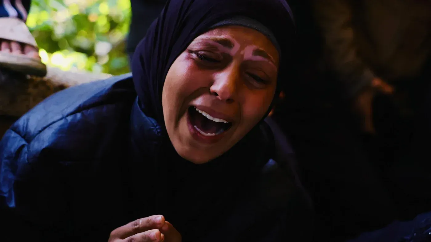 امرأة ترتدي الحجاب تعبر عن حزن عميق أثناء تأبين ضحايا الحرب في غزة، مع خلفية غير واضحة تعكس مشاعر الألم والمعاناة.