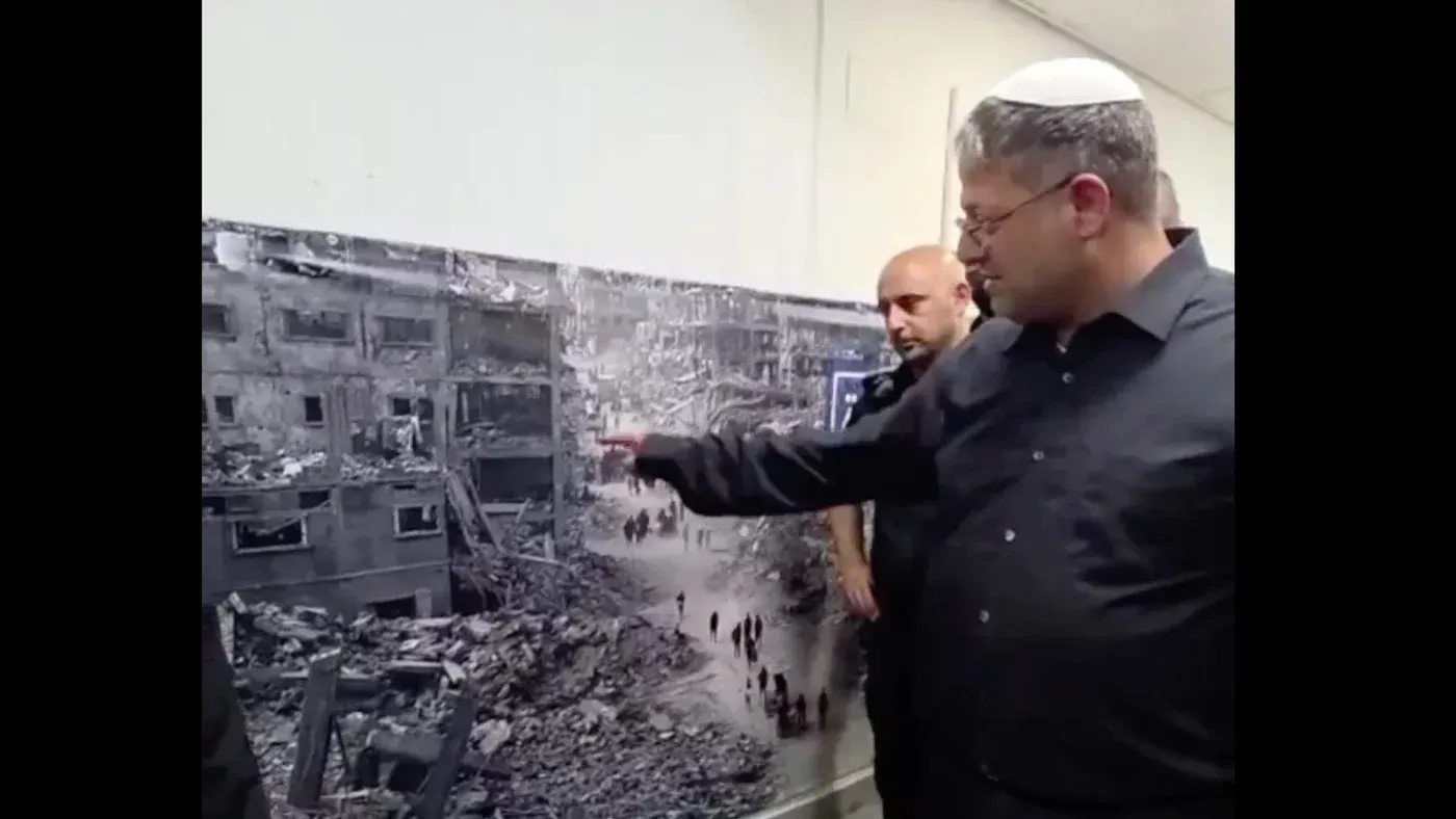وزير الأمن القومي الإسرائيلي إيتامار بن غفير يشير بفخر إلى صورة كبيرة لمبانٍ مدمرة في غزة، بينما يقف بجانبه آخرون.