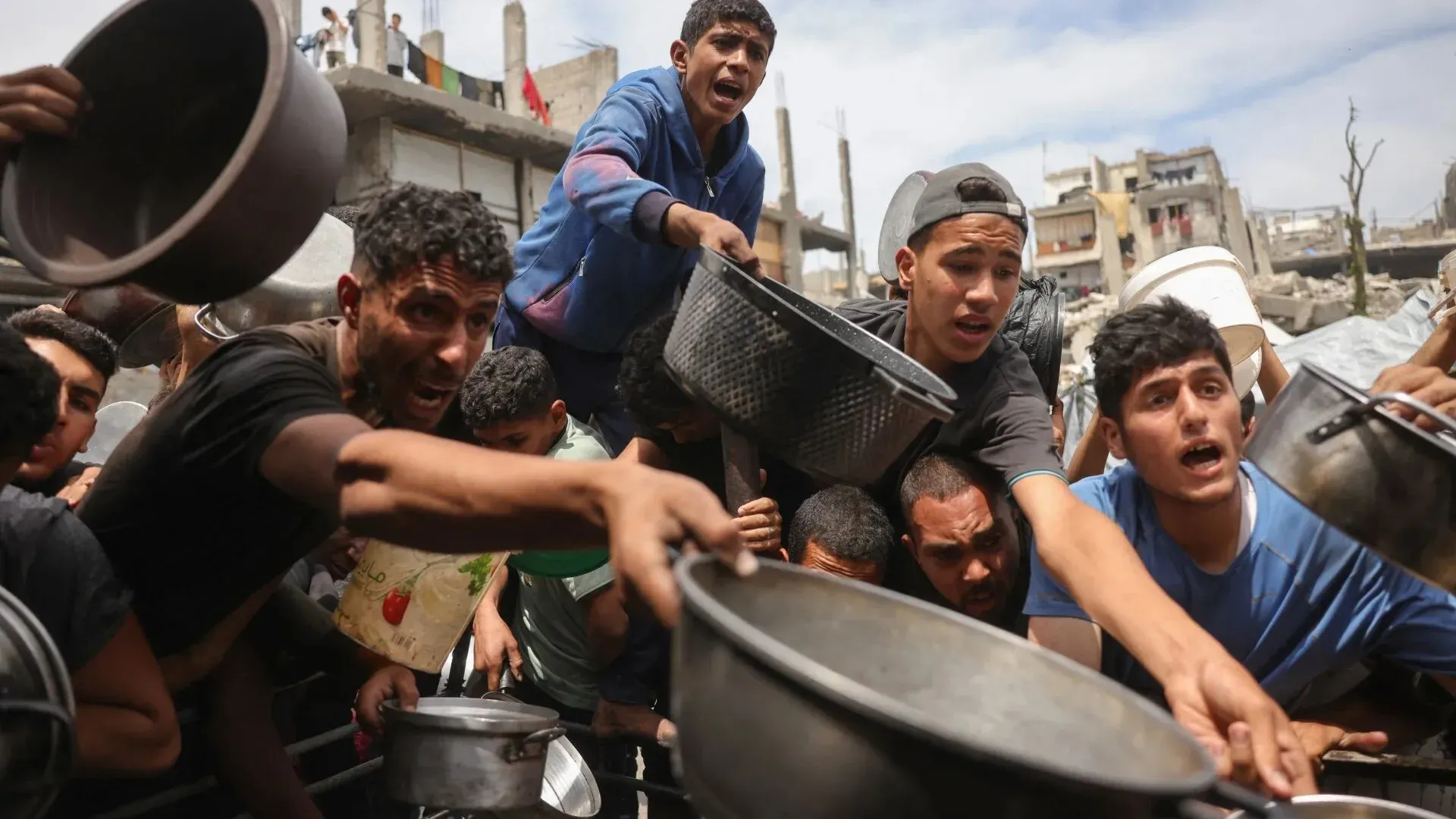 شباب فلسطينيون يتزاحمون للحصول على الطعام في غزة، وسط دمار هائل، في ظل أزمة إنسانية خانقة بسبب الحصار الإسرائيلي.