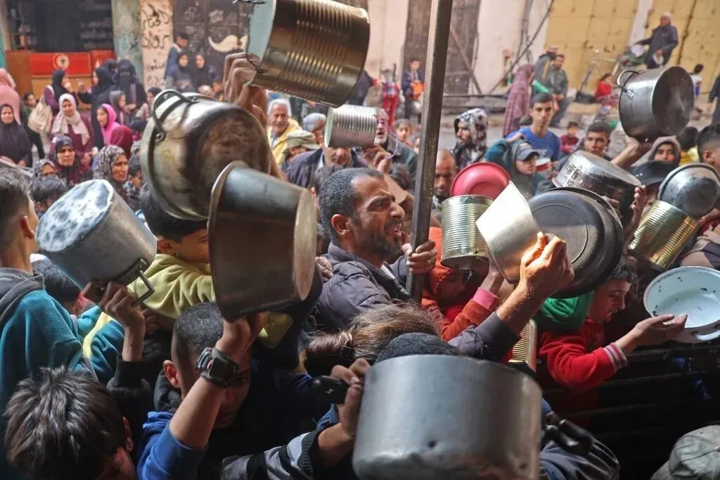 حشد كبير من الفلسطينيين في غزة يحملون أواني معدنية أثناء انتظارهم للحصول على المساعدات الغذائية، وسط أجواء من التوتر والقلق.
