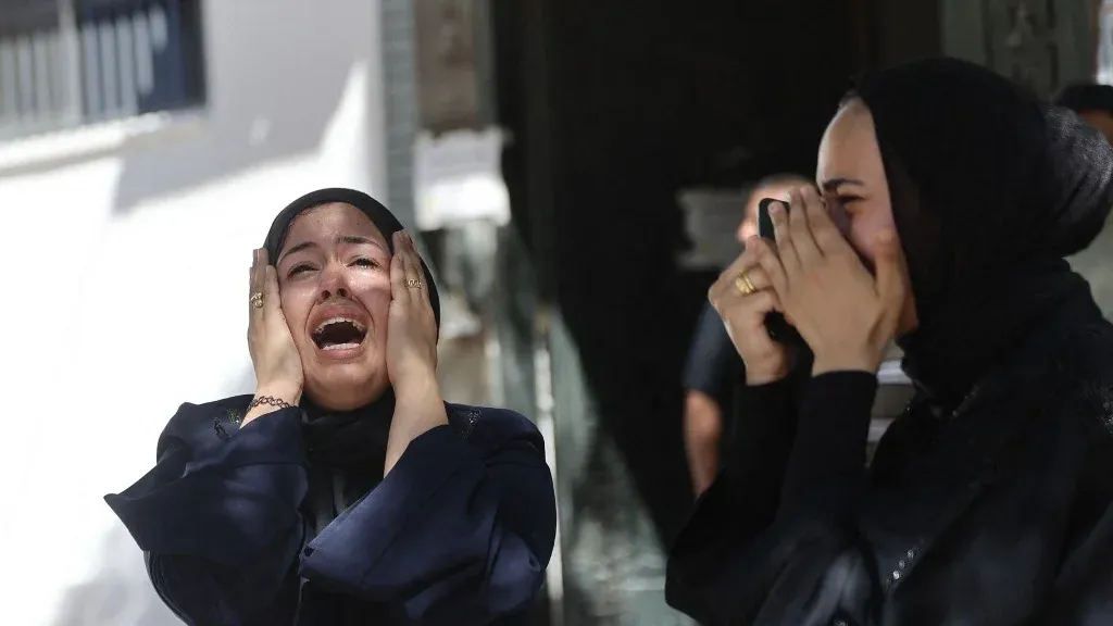 امرأتان ترتديان الحجاب تعبران عن حزن شديد بالبكاء في مشهد يعكس مأساة المدنيين الفلسطينيين في غزة جراء إطلاق النار الإسرائيلي.