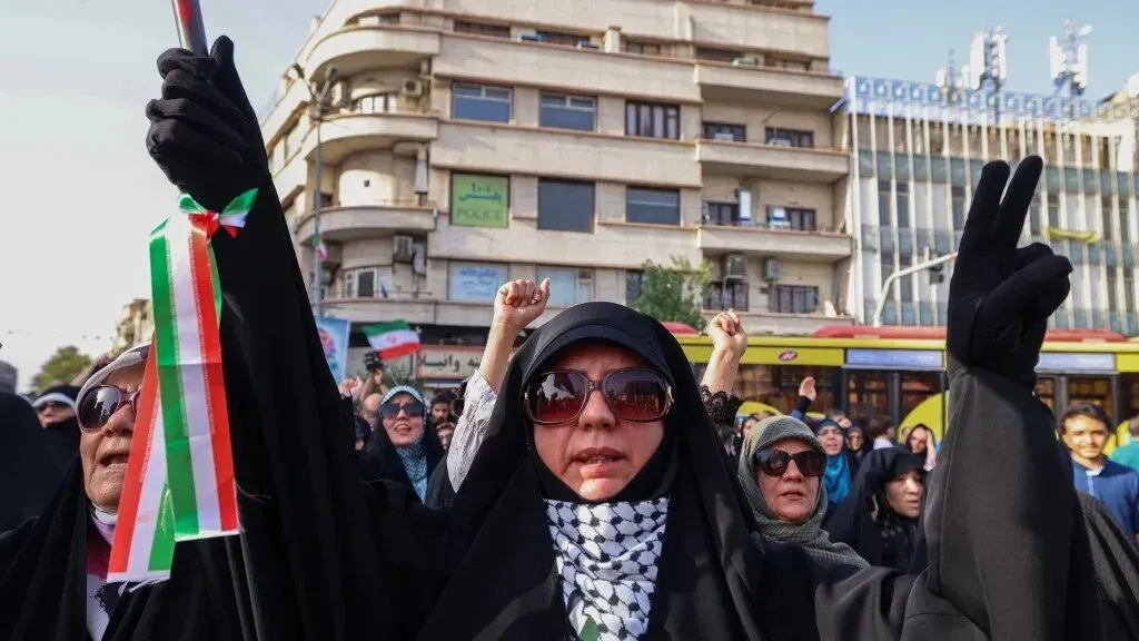 نساء يرتدين الحجاب ويحتفلن في تجمع حاشد، يحملن أعلامًا إيرانية ويعبرن عن دعمهن للوطن، في سياق الأحداث الجارية.