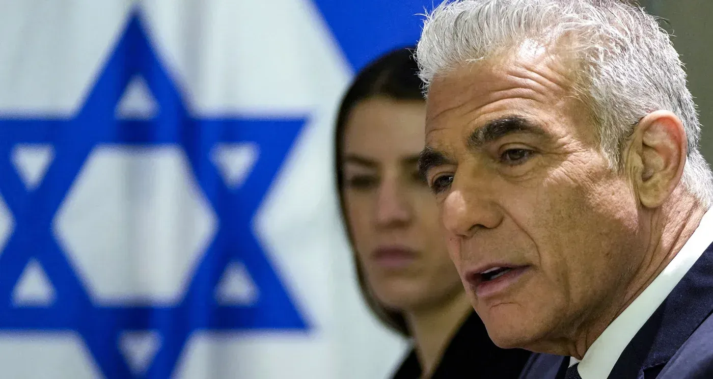 يائير لبيد يتحدث في مؤتمر صحفي، خلفه علم إسرائيل، مع التركيز على التوترات بين إيران وفنزويلا والولايات المتحدة.