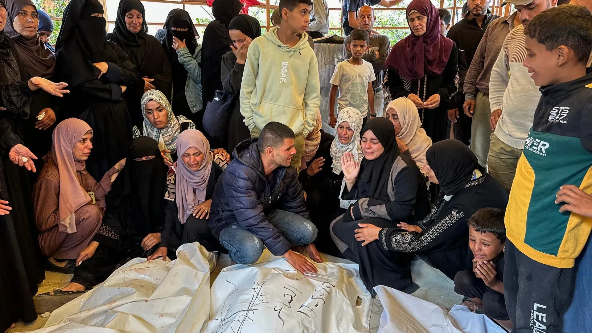 مجموعة من الأشخاص في حالة حزن شديد حول جثمان مغطى، بينما يتجمع الأهل والأصدقاء في مشهد مؤثر في غزة.