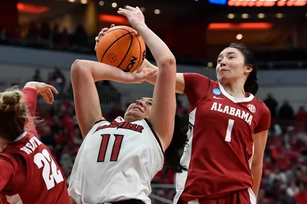 لاعبة كرة سلة من فريق لويزفيل تحاول تسجيل نقطة بينما تتصدى لها لاعبة من فريق ألاباما خلال مباراة NCAA المثيرة.