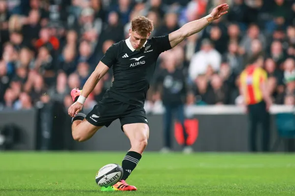 لاعب رغبي نيوزيلندي من فريق All Blacks يركل الكرة خلال مباراة اختبار ضد جنوب أفريقيا، مع جمهور في الخلفية.