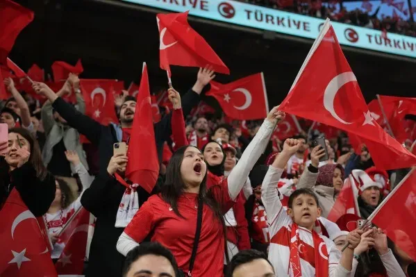 جماهير تركية تحتفل في الملعب، تحمل الأعلام وتظهر حماسها خلال مباراة تصفيات كأس العالم، تعبيراً عن دعمها للمنتخب الوطني.