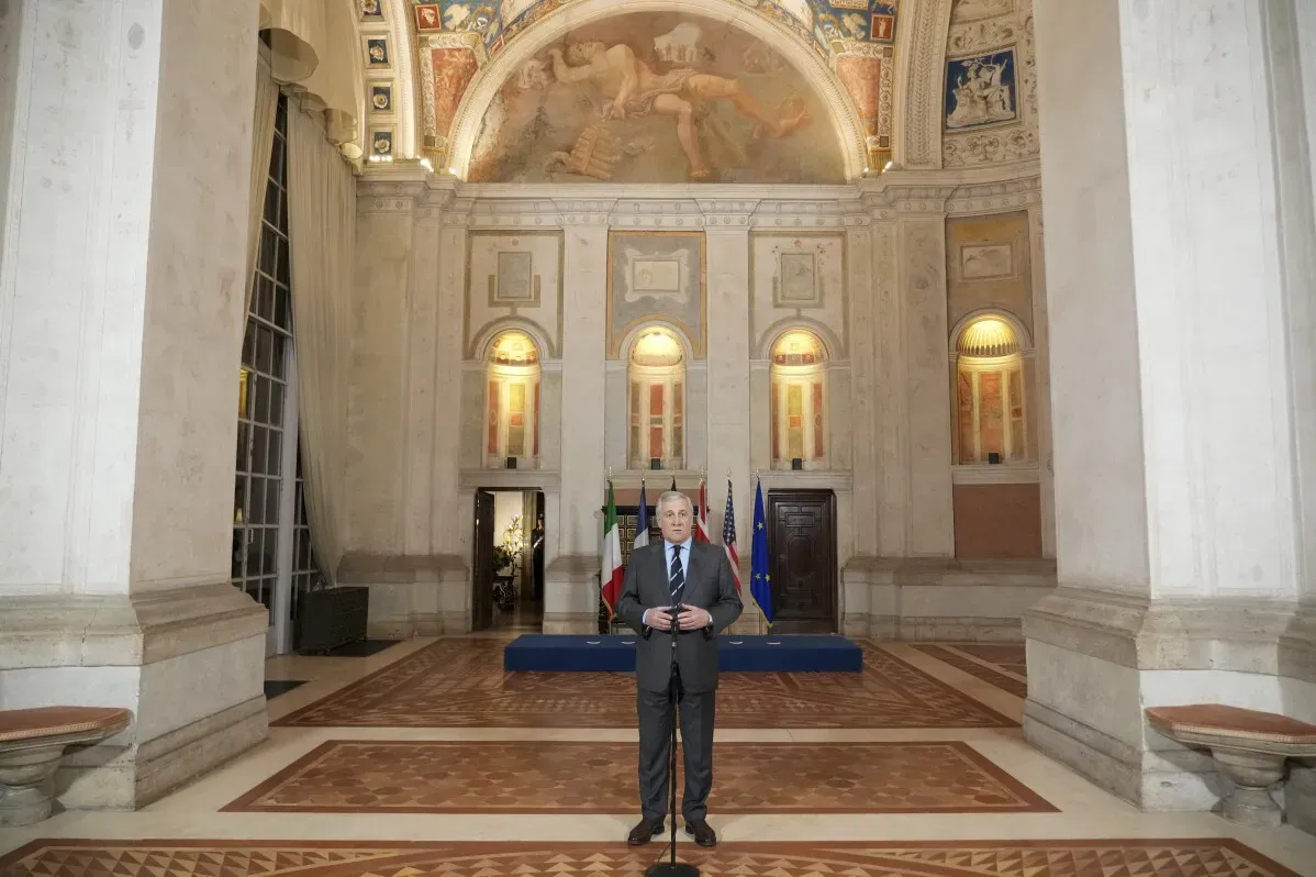 وزير الخارجية الإيطالي أنطونيو تاجاني يتحدث في قاعة رسمية، مع أعلام دولية خلفه، حول الوضع السياسي في سوريا.