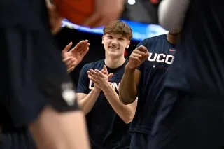 برايلون مولينز، لاعب كرة سلة في فريق UConn، مبتسمًا أثناء التحضيرات للمباراة، مع زملائه في الفريق خلفه.