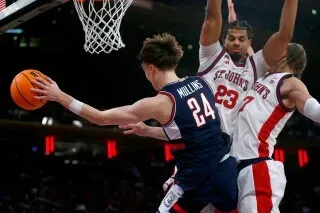 برايلون مولينز، لاعب كرة السلة في فريق يوكون، يسدد الكرة أثناء مواجهة فريق سانت جون، مع وجود لاعبين مدافعين يحاولون إعاقة تسديدته.