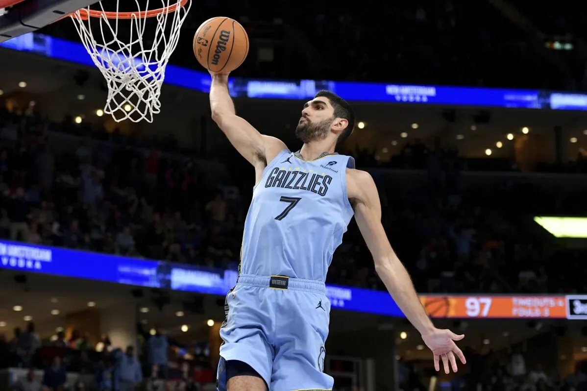 لاعب كرة سلة من فريق ممفيس جريزليز ينفذ تسديدة ساحقة خلال مباراة ضد فينيكس صنز، مع ظهور الجماهير في الخلفية.