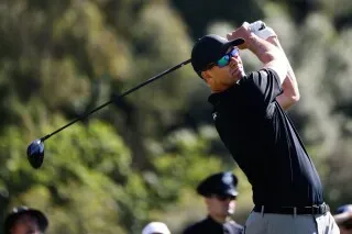 جاكوب بريدجمان يسدد ضربة جولف في بطولة جينيسيسيس إنفيتيشنال، مع خلفية طبيعية وجمهور يشاهد.