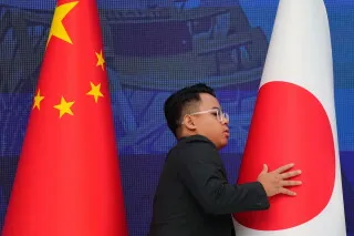 رجل يلمس العلم الياباني بجانب العلم الصيني في سياق التوترات الاقتصادية بين بكين وطوكيو حول استيراد مادة ثنائي كلوريد السيلان المستخدمة في رقائق أشباه الموصلات.
