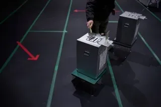 ناخب يضع صوته في صندوق اقتراع خلال الانتخابات البرلمانية في طوكيو، مع وجود علامات توجيه على الأرض.