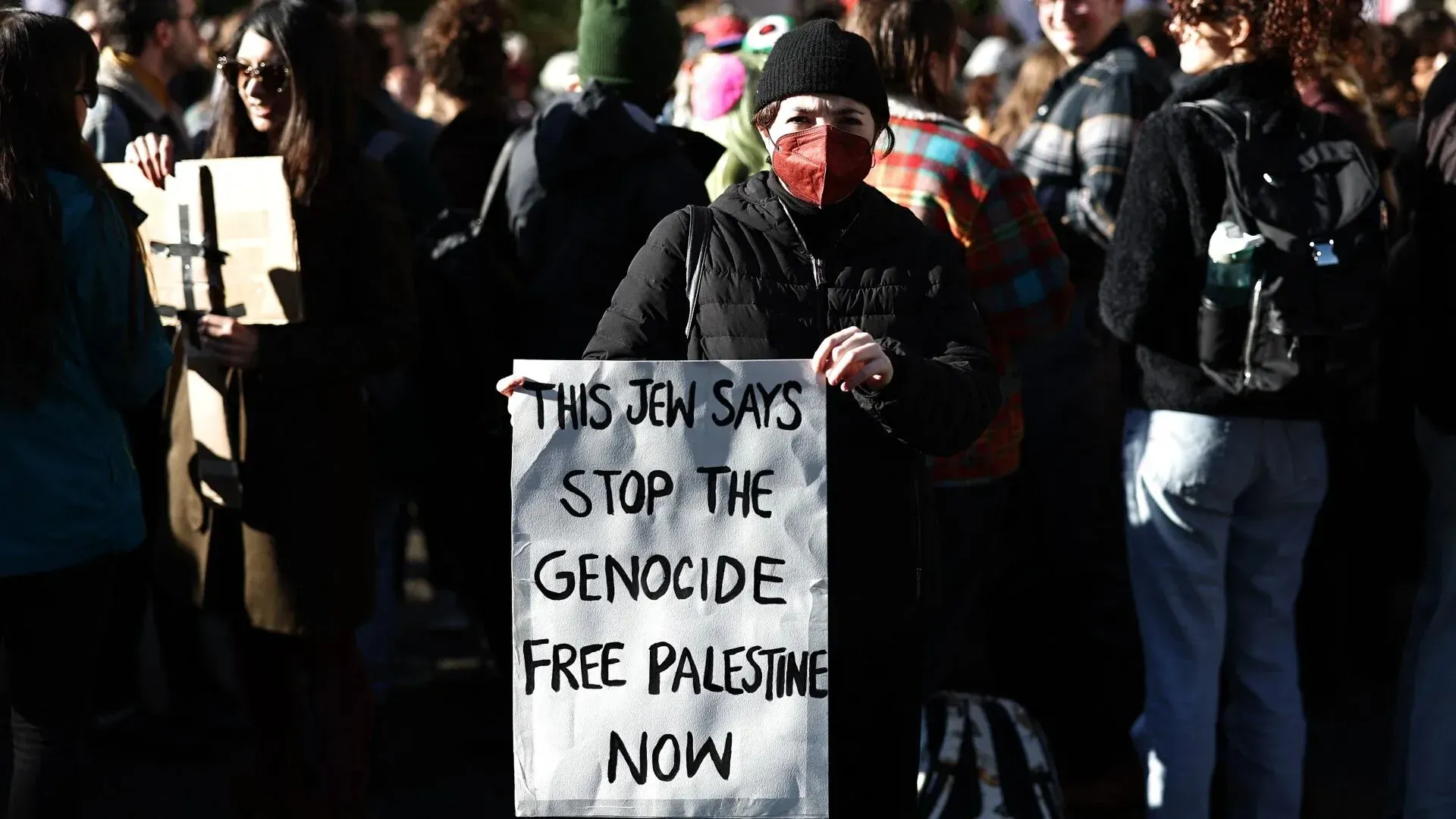 امرأة تحمل لافتة مكتوب عليها "هذا يهودي يقول: توقفوا عن الإبادة، فلسطين حرة الآن" وسط حشد من المتظاهرين.