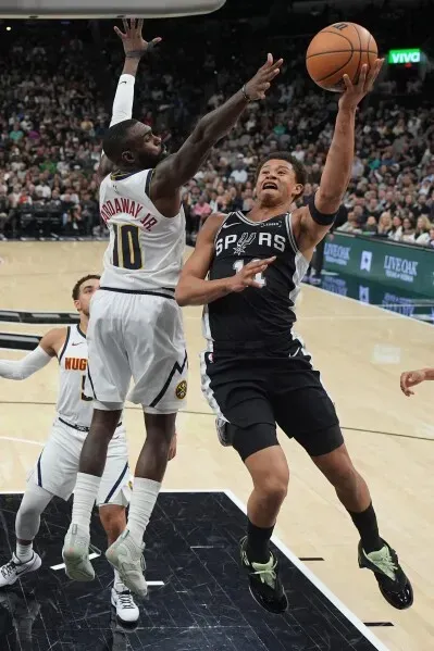 لاعب سان أنطونيو ستيفون كاسل يسجل سلة تحت ضغط من مدافع دنفر، مع وجود لاعبين آخرين في الخلفية خلال مباراة مثيرة في الدوري الأمريكي للمحترفين.