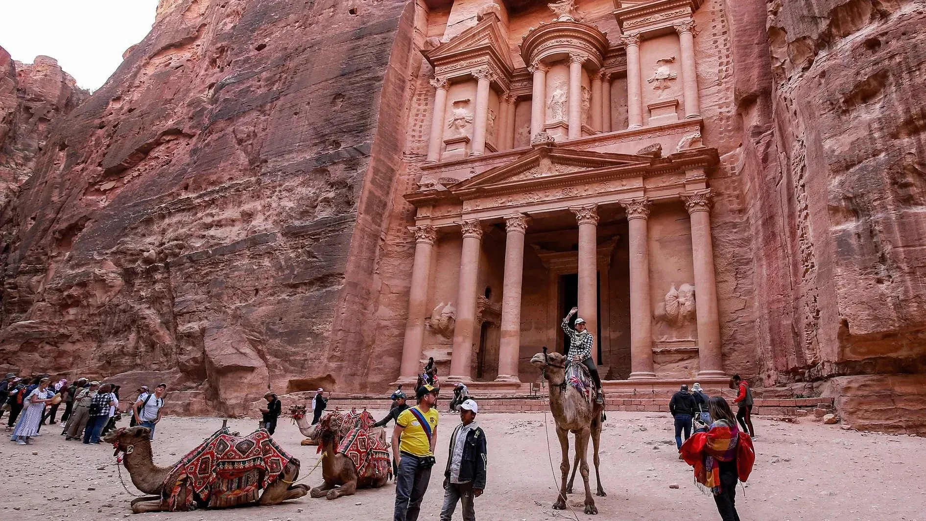 مشهد من البتراء يظهر السياح يستكشفون الموقع الأثري، مع جمال المعمار الفريد والجبال المحيطة.