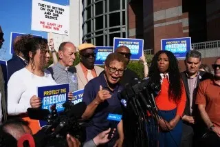 مجموعة من المتحدثين في مؤتمر صحفي، يتحدثون عن حرية الصحافة بعد اعتقال الصحفي دون ليمون، مع لافتات تدعو لحماية حقوق الإعلام.