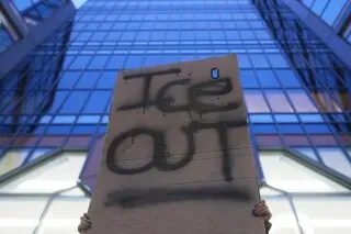 لافتة مكتوبة عليها "ICE OUT" تُرفع أمام مبنى زجاجي، تعبيرًا عن الاحتجاج ضد سياسة الهجرة.