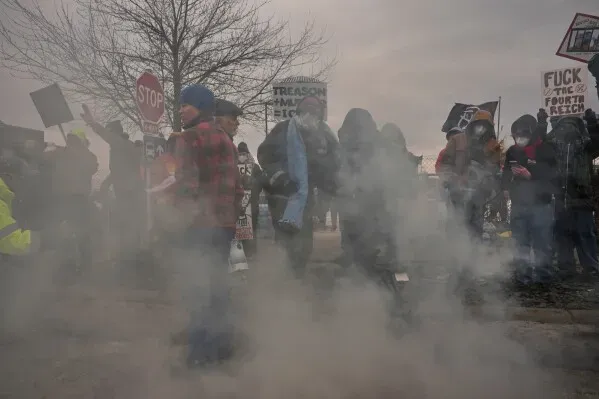 متظاهرون في مينيابوليس يتجمعون وسط دخان الغاز المسيل للدموع، حاملين لافتات تعبر عن احتجاجاتهم ضد إنفاذ قوانين الهجرة.