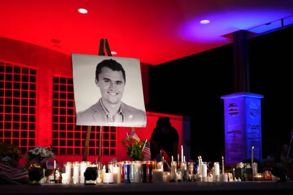 صورة لشمع وورود وأعلام صغيرة أمام صورة الناشط المحافظ Charlie Kirk في نصب تذكاري بعد مقتله بولاية يوتا.