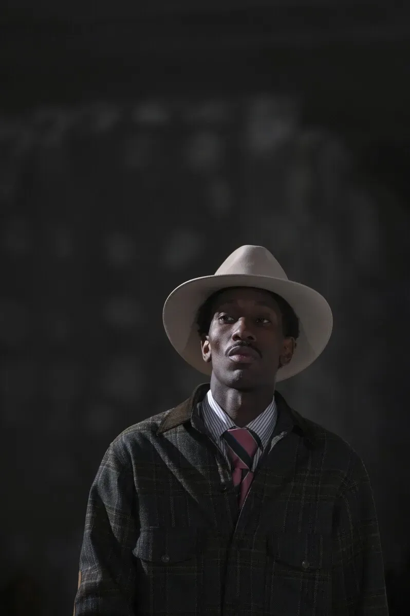 رجل يرتدي سترة عصرية وقبعة واسعة، يظهر في عرض أزياء بجو مفعم بالألوان والقطع الغريبة، تعبيراً عن الأسلوب الطليعي لجونيا واتانابي.