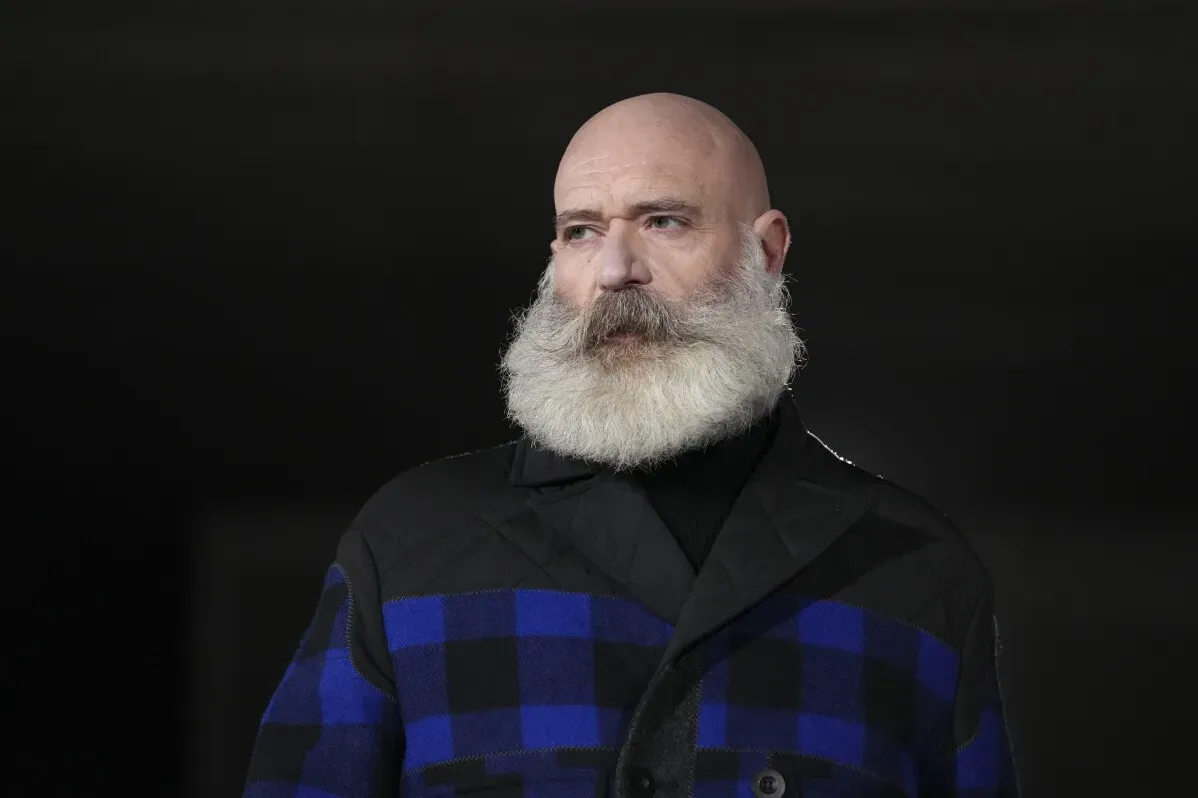 رجل ذو لحية بيضاء يرتدي معطفاً مزركشاً بالأزرق والأسود، يعكس أسلوب موديلات جونيا واتانابي للأزياء الطليعية.