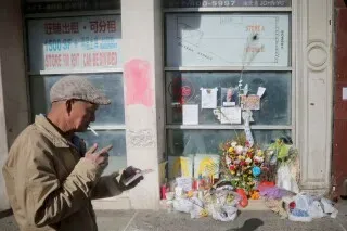 رجل مسن يدخن سيجارة ويقف أمام نصب تذكاري في حي الصيني بنيويورك، حيث وضعت الزهور والرسائل تخليدًا لذكرى الضحايا.