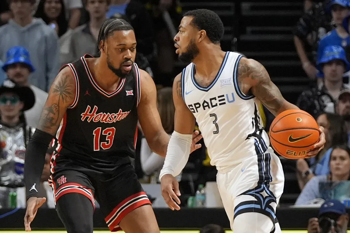 لاعب هيوستن رقم 13 يواجه لاعب UCF رقم 3 خلال مباراة كرة سلة مثيرة، مع الكرة على استعداد للتسديد في لحظة حاسمة.