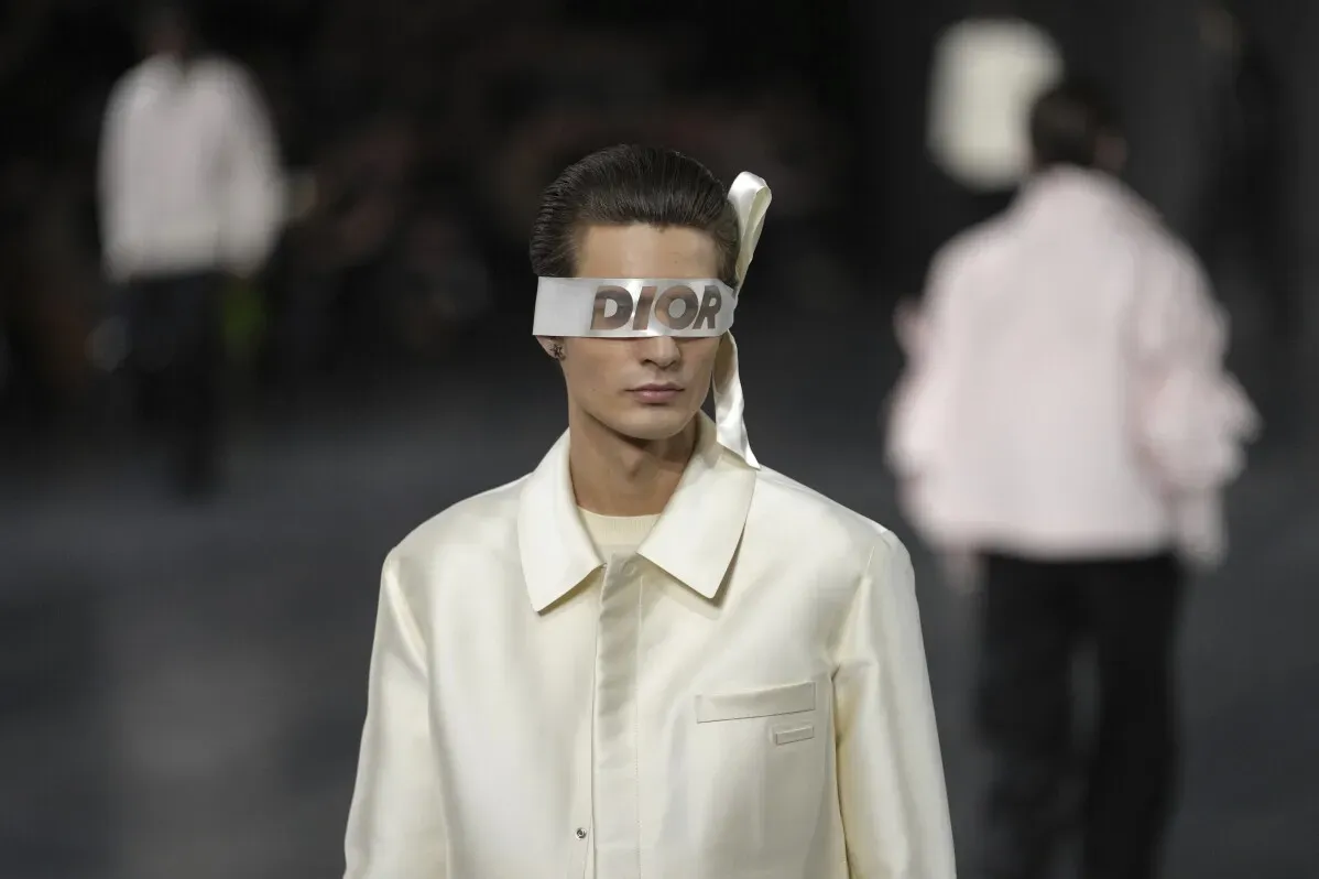 عارض أزياء يرتدي قميصًا كريميًا مع نظارات تحمل شعار "DIOR"، بينما يسير في عرض ديور خلال أسبوع الموضة في باريس.