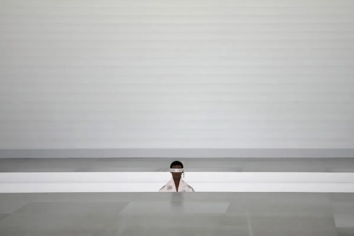 عارض أزياء في عرض ديور للرجال، وسط تصميم بسيط وزاوي، يعكس التحول نحو الذكورية التقليدية في الموضة.