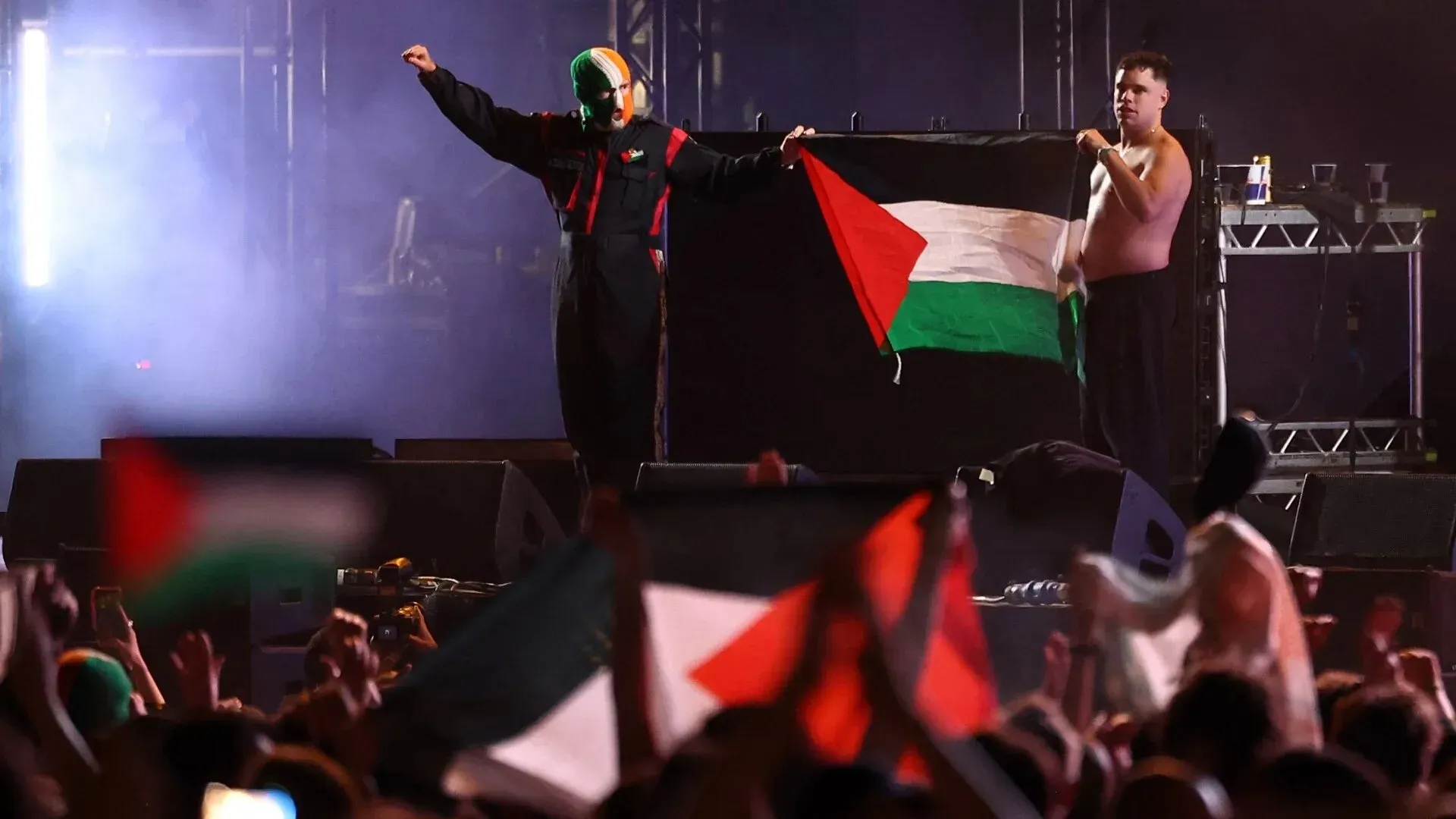فرقة "كنيكاب" تعرض علم فلسطين على المسرح خلال حفل في لندن، مع تفاعل حماسي من الجمهور الذي يحمل الأعلام.
