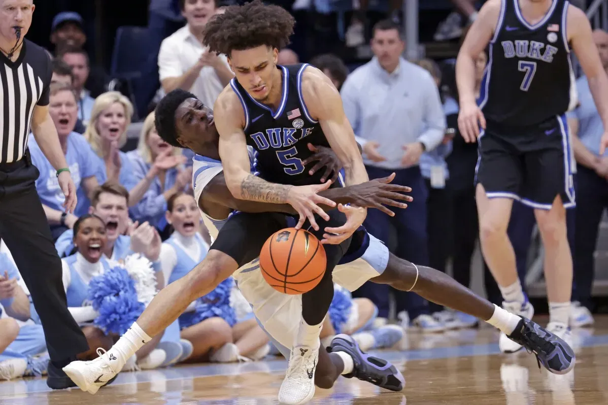 لاعب ديوك كون كنوبل يتصارع مع لاعب UNC على الكرة خلال مباراة حماسية، مع تواجد الجماهير في الخلفية.