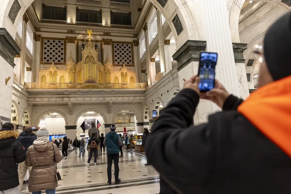 زوار يتجولون في قاعة تاريخية، مع شخص يلتقط صورة لهاتفه أمام آلة موسيقية كبيرة، تعكس تراجع مبيعات المتاجر.