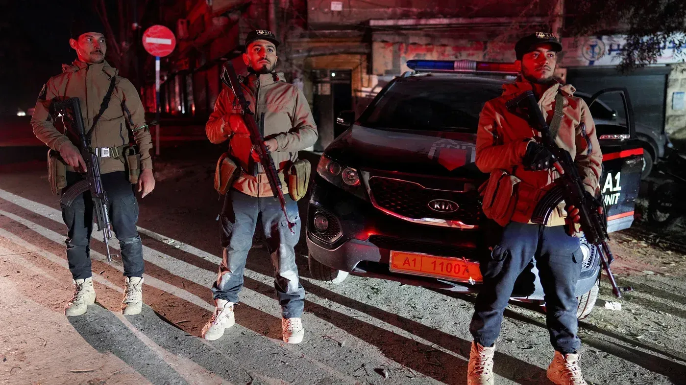 عناصر من القوات الكردية يقفون مسلحين في شارع الأشرفية بحلب، بينما تظهر سيارة أمنية خلفهم، وسط أجواء من التوتر بعد الهدنة.