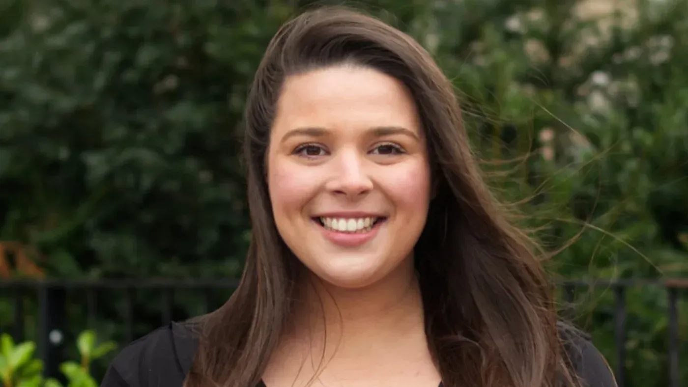 إيزي لينغا، عضوة في مجلس مدينة لندن، تظهر مبتسمة في صورة رسمية، مع خلفية خضراء، تمثل دورها في السياسة المحلية.