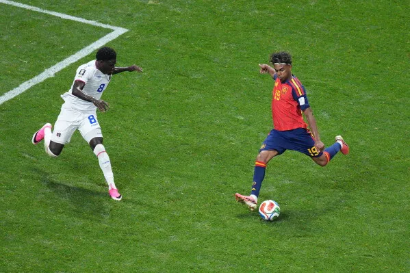 لاعب إسباني يتقدم بالكرة في مباراة كأس العالم، بينما يحاول لاعب منافس منعه من التقدم، مع التركيز على مهارات Yamal الشابة.