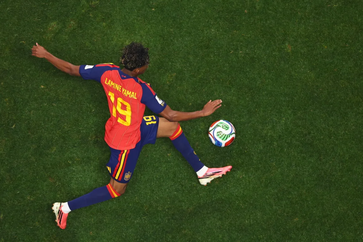 لاعب المنتخب الإسباني لامين يامال، رقم 19، في وضعية استعداد للعب الكرة خلال مباراة كأس العالم، مع التركيز على تفاصيل زيّه الرياضي.