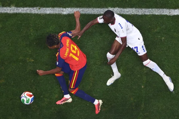لاعب إسباني شاب يرتدي القميص رقم 19 يتعرض للعرقلة من لاعب آخر خلال مباراة في كأس العالم، مع التركيز على حركته الديناميكية.