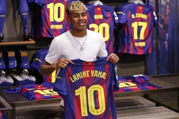لامين يامال يحمل قميص برشلونة رقم 10 في متجر النادي، مع خلفية من القمصان الأخرى، معبرًا عن طموحاته في السير على خطى الأساطير.