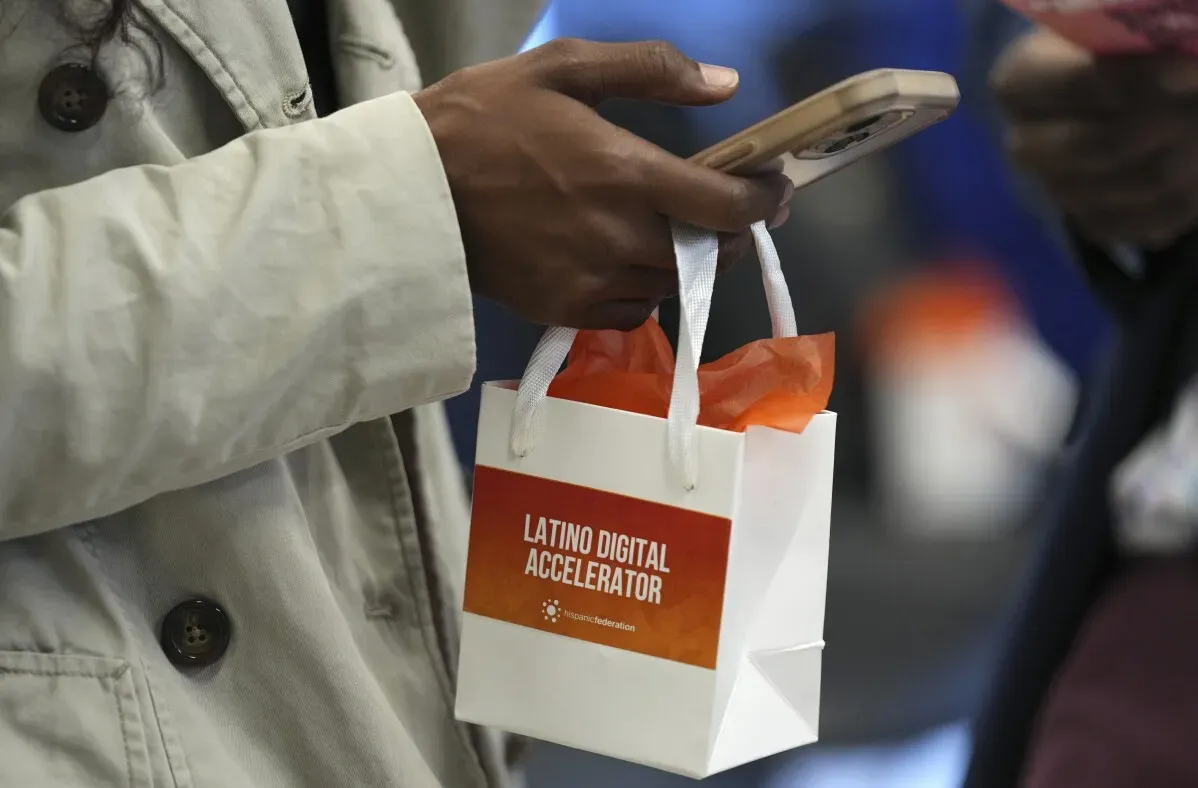 حقيبة تحمل شعار "Latino Digital Accelerator" تُمسك بيد شخص يستخدم هاتفه المحمول، تعكس أهمية المهارات الرقمية للعمال اللاتينيين.