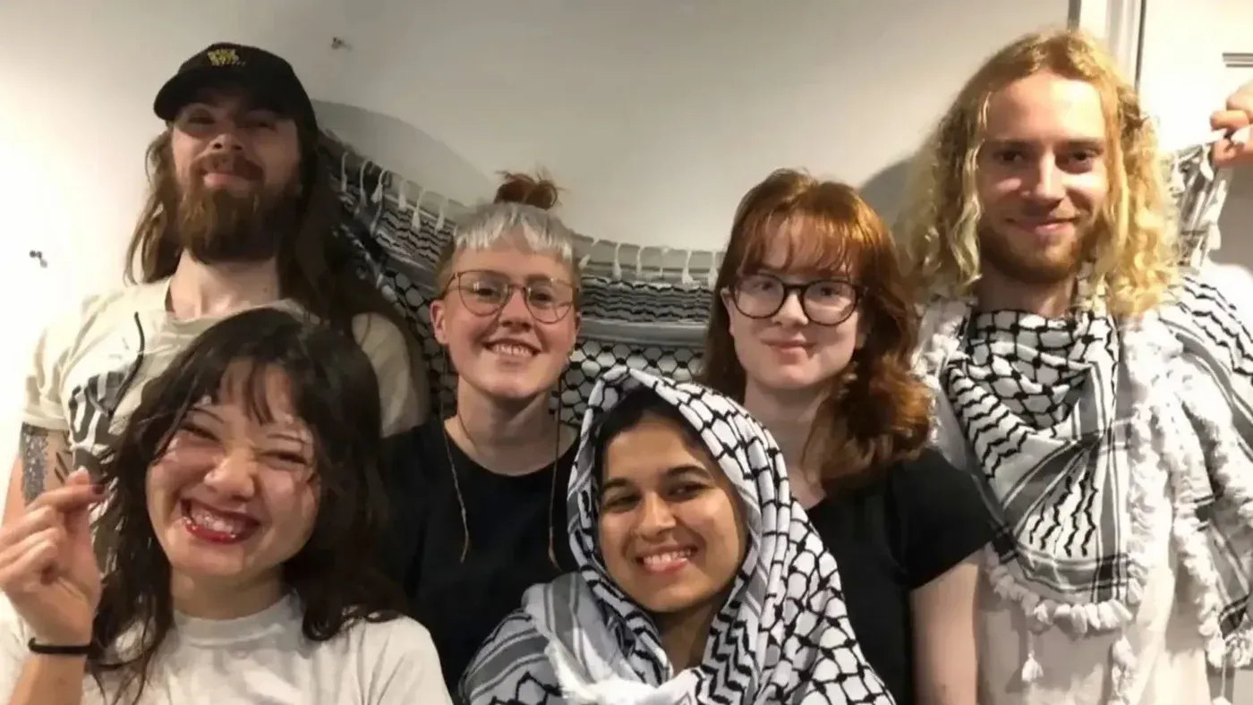 مجموعة من النشطاء يرتدون الكوفية الفلسطينية، يبتسمون معًا في صورة جماعية تعكس تضامنهم مع القضية الفلسطينية.