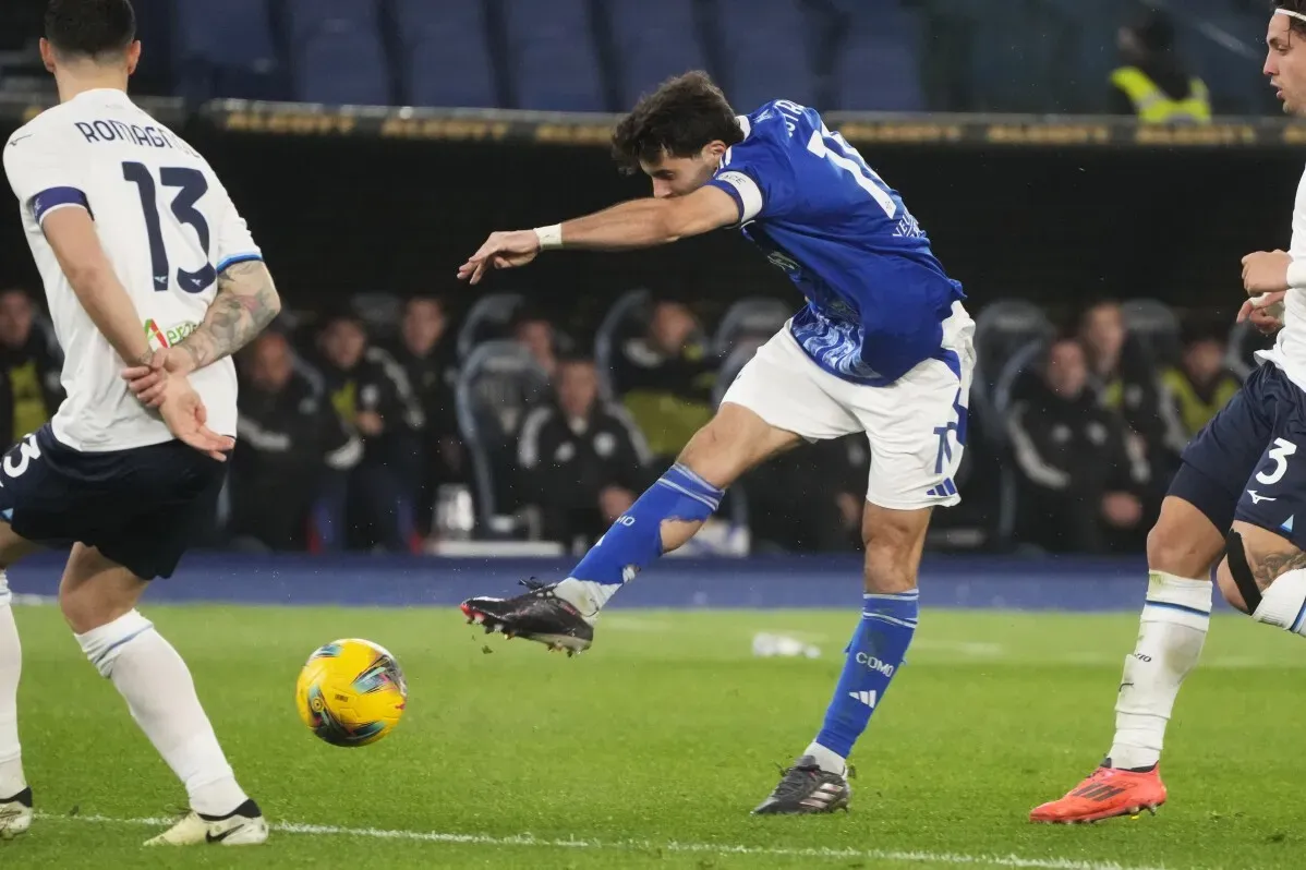 لاعب من نادي كومو يسدد الكرة نحو المرمى أثناء مباراة الدوري الإيطالي ضد لاتسيو، مع وجود لاعبين آخرين في الخلفية.