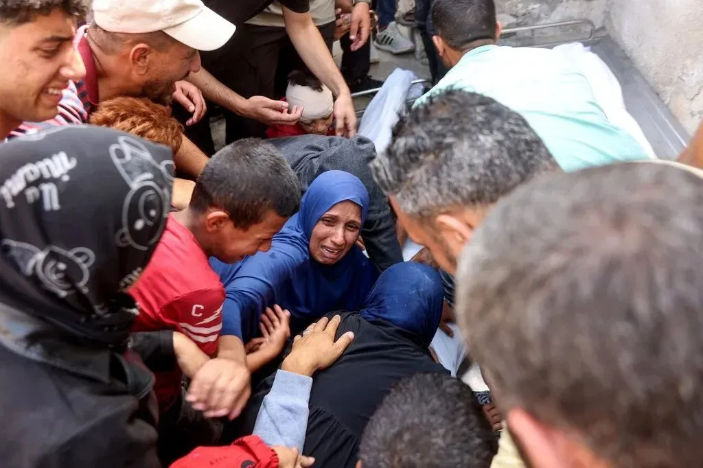 مواطنون فلسطينيون يتجمعون حول امرأة تبكي، تأثراً بفقدان أحد أفراد عائلتها في أحداث العنف في غزة. تعكس الصورة الألم والمعاناة المستمرة.