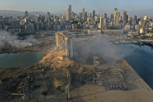 دمار هائل في مرفأ بيروت بعد انفجار 4 أغسطس 2020، مع بقايا المباني المدمرة والدخان يتصاعد، مشهد يرمز إلى الكارثة.